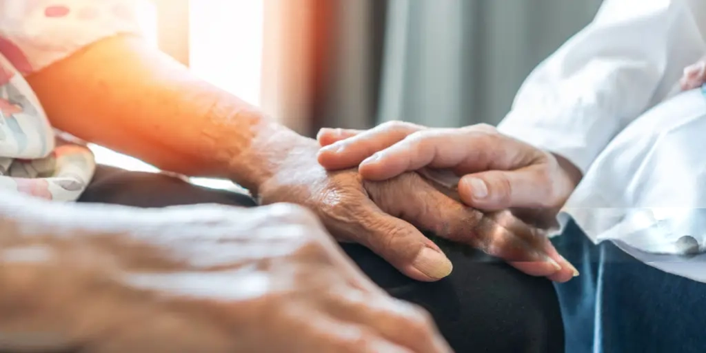 A caregiver holding the hand of an elderly client at home